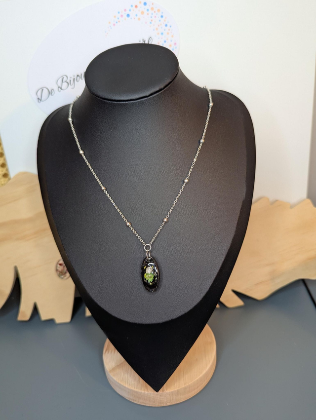 Collier mi long avec une chaine de couleur argent et un pendentif en résine noire avec des fleurs séchés. 