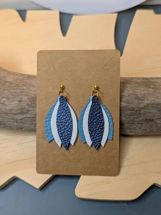 Boucles d'oreilles en cuir en forme de fleur de couleur bleu et blanc le derrière est en tissu enduit, le fermoir clou est en or.