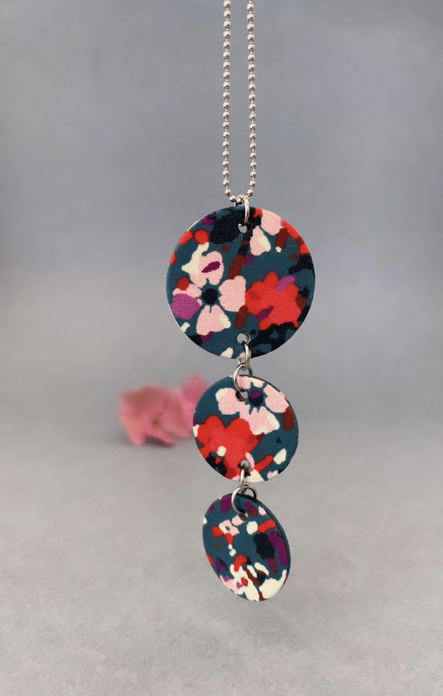 Collier avec pendentif en carton et tissu imprimé, composé de trois cercles, collection "anémones", fond bleu et motifs fleuris rose, rouge, blanc.  
