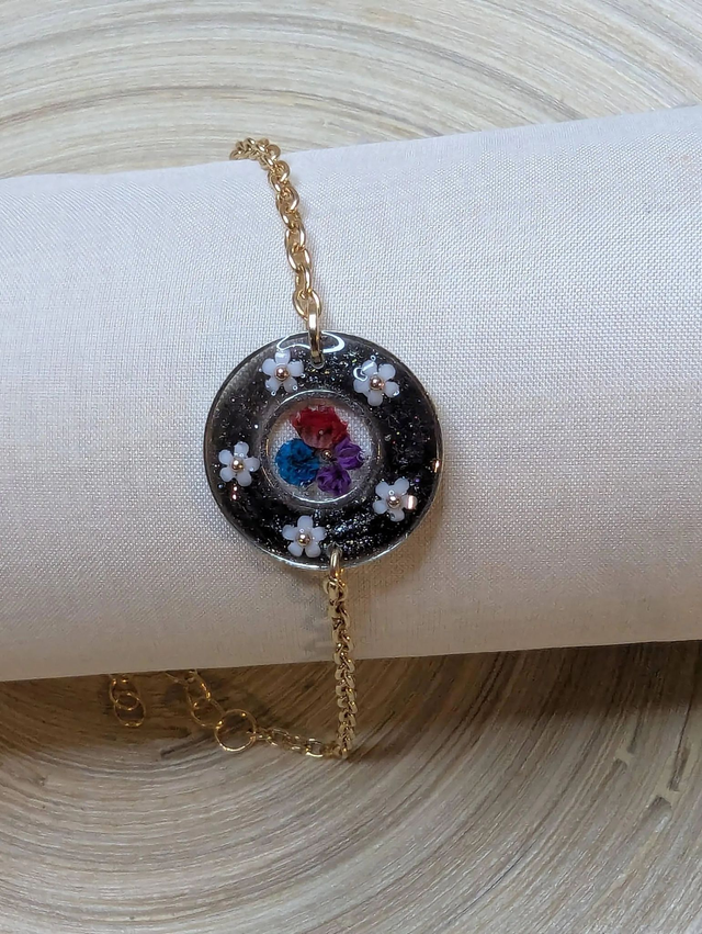 Bracelet avec une chaine de couleur or, le pendentif est en résine noir avec des fleurs séchés, le fermoir est en or. 
