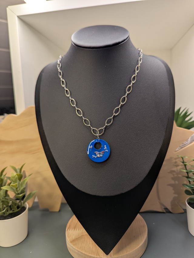 Collier avec une chaine de couleur argent et un pendentif rond  en résine bleu. 