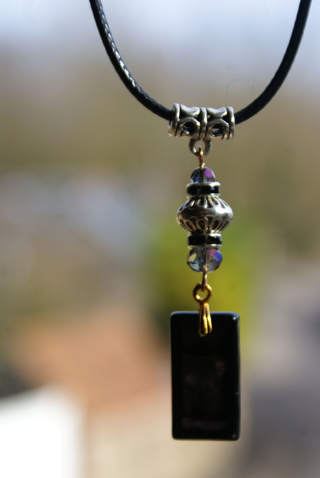 Pendentif en verre noir iridescent et cordon en coton ciré noir.