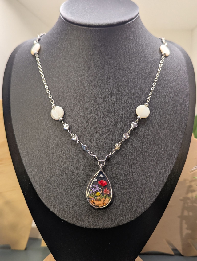 Collier mi long avec deux chaines de couleurs argent, des perles de nacre et un pendentif en résine avec fleurs séchés. 