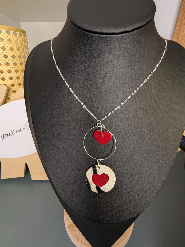 Collier long, sautoir, avec une chaine de couleur argent, un pendentif en cuir et en tissus enduit en forme de rond et de cœur