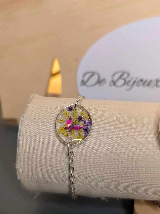Bracelet avec une chaine de couleur argent, un pendentif en résine avec des fleurs séchés et un papillon en stickers, le fermoir est en argent. 
