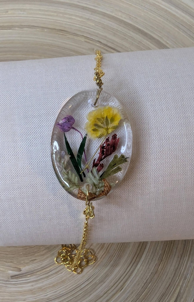 Bracelet avec une chaine de couleur or, le pendentif est en résine avec des fleurs séchés jaune et violet, le fermoir est en or.