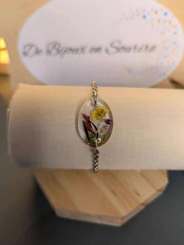  Bracelet avec une chaine de couleur argent et un pendentif en résine avec des fleurs séchés jaune, le fermoir est en argent. 
