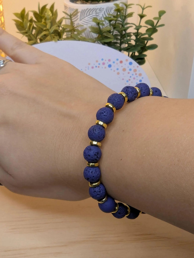 Bracelet en pierre de lave bleu foncé, avec des perles d'espacement doré. Le fermoir et la chaine fermoir sont de couleur or.