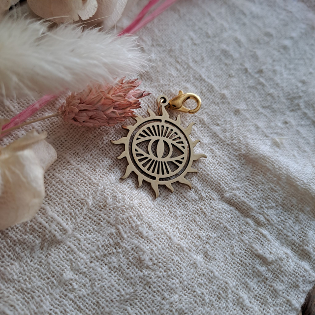 Charms colorie dorée en forme de rond avec un oeil dedant