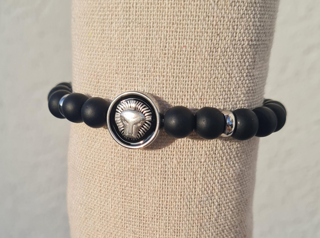 Bracelet élastique unisexe en pierre onyx mat avec séparateurs et perle centrale plate "lion" en acier inoxydable argenté sur fond noir.