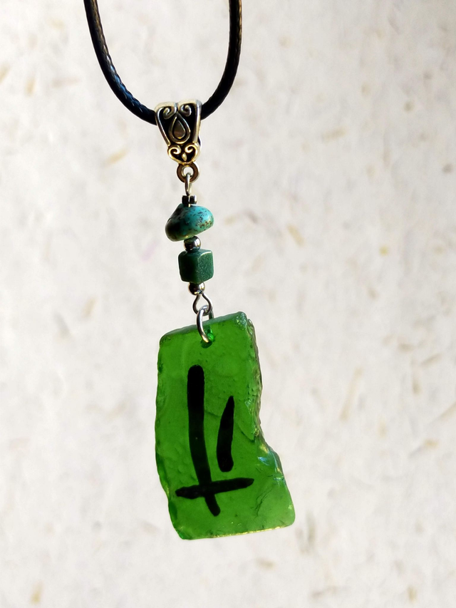 Pendentif en verre vert texturé avec motif peint et chaîne en coton ciré noir.