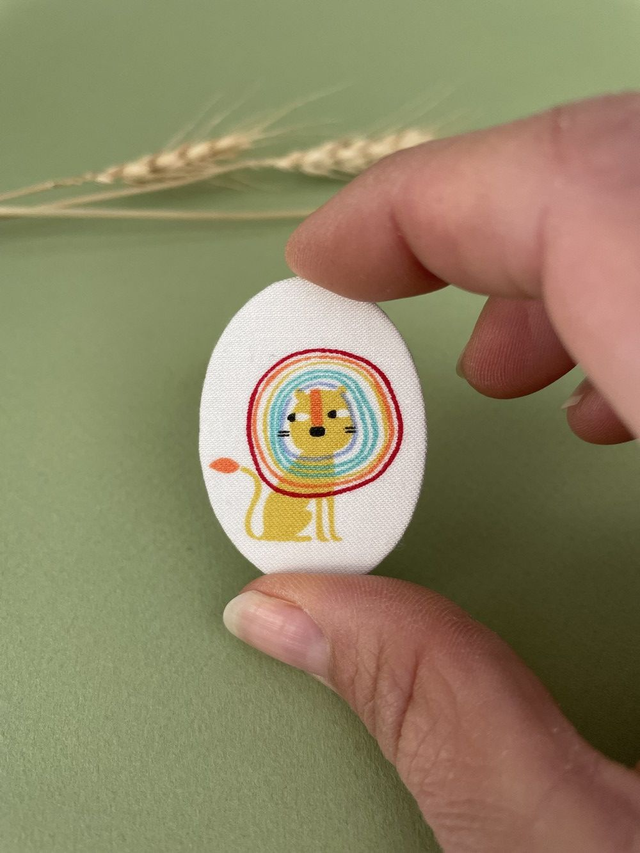 Broche ovale lion crinière arc-en-ciel en carton et tissu imprimé