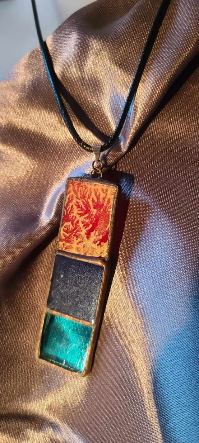 Pendentif en pâtes de verres bleu transparent, bleu opaque et rouge opaque sertis en Tiffany . Chaîne en coton ciré noir. 