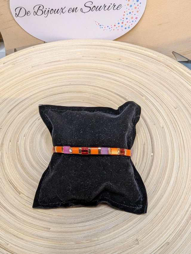 Bracelet avec des perles plate en verre rose, orange et des petites en métal doré. Le fermoir et la chaine fermoir sont en or.