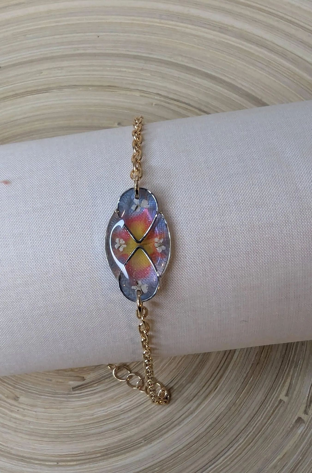 Bracelet avec une chaine de couleur or, pendentif en résine bleu, rose et jaune avec des petites fleurs blanches, le fermoir est en or.