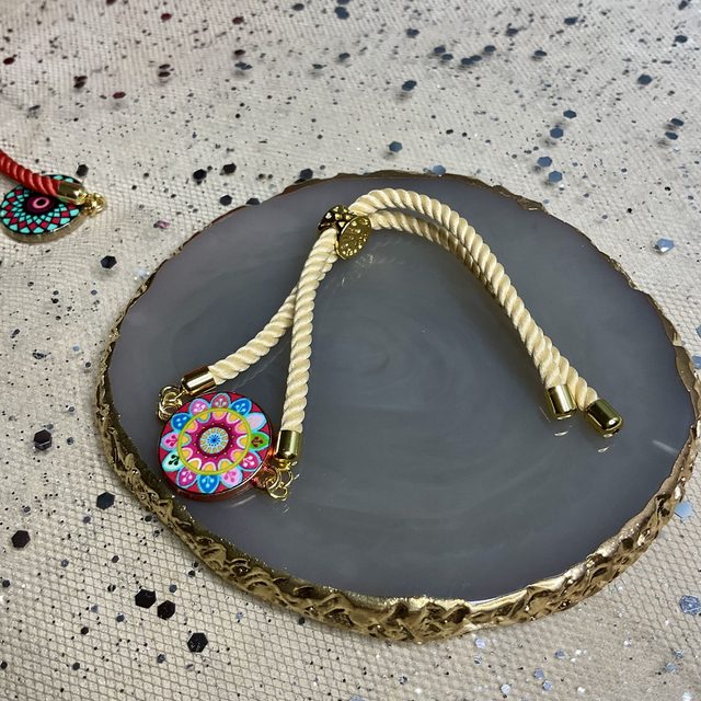 Fully adjustable cord bracelet with enamel charm.