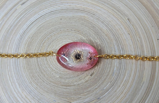 Bracelet avec une chaine de couleur or et un pendentif en résine rose transparent, motif fleur, le fermoir est en or.