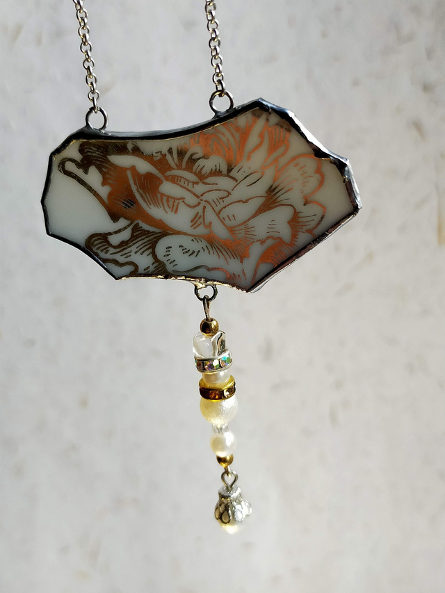 Pendentif en faïence blanche avec motif floral doré serti en Tiffany. 