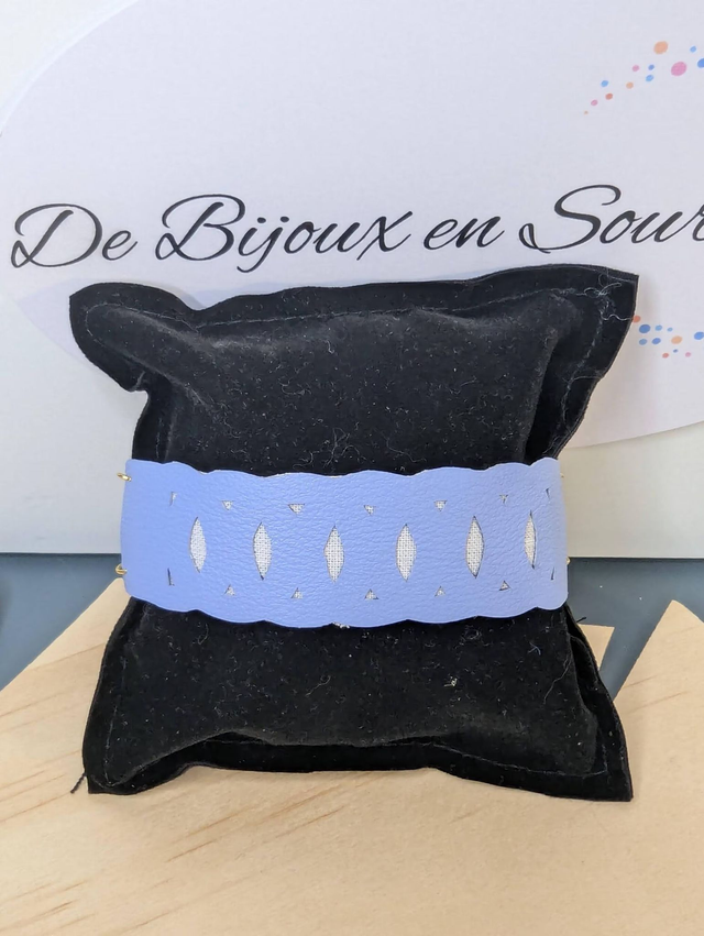 Bracelet manchette en cuir bleu lisse, avec du tissus enduit blanc (résistant), une chaine dorée. Le fermoir est de couleur or. 