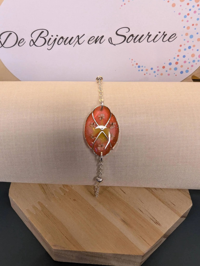 Bracelet avec une chaine de couleur argent, un pendentif résine rose et jaune avec fleurs, le fermoir est en argent. 