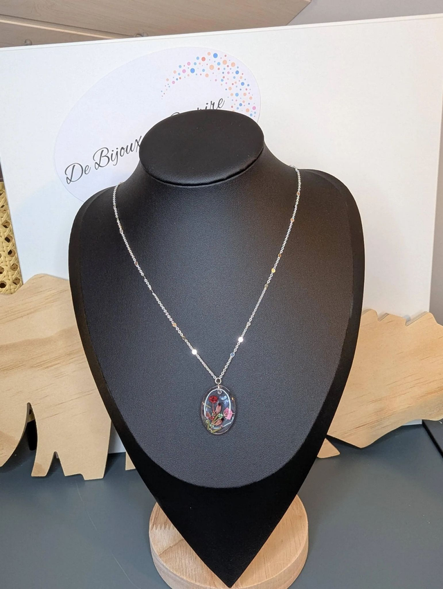 Collier mi long avec une chaine de couleur argent et un pendentif en résine avec des fleurs séchés rouge et rose. 
