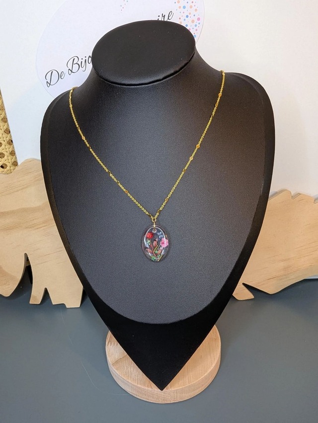 Collier mi long avec une chaine en couleur or et un pendentif en résine avec des fleurs séchés rouge et rose. 