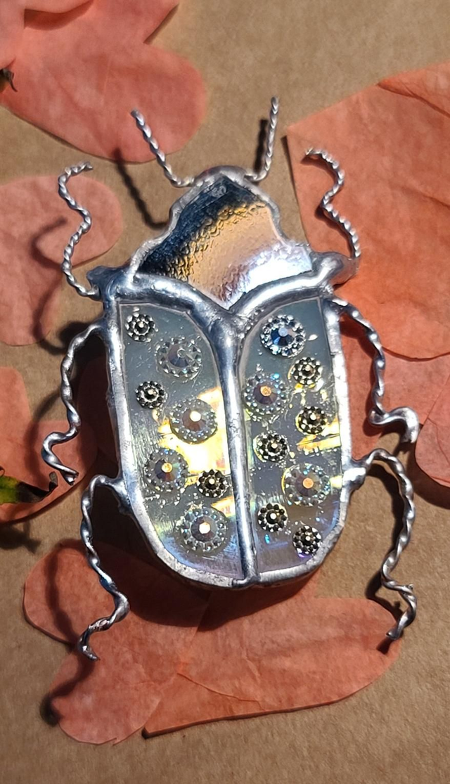 Scarabée en Tiffany, au corps blanc iridescent et à la tête noire et monté en broche. 