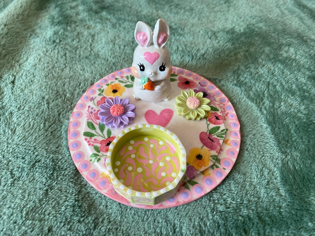 Osterhäschen sitzend auf einem Teller mit Blumen und einem Kerzenständer