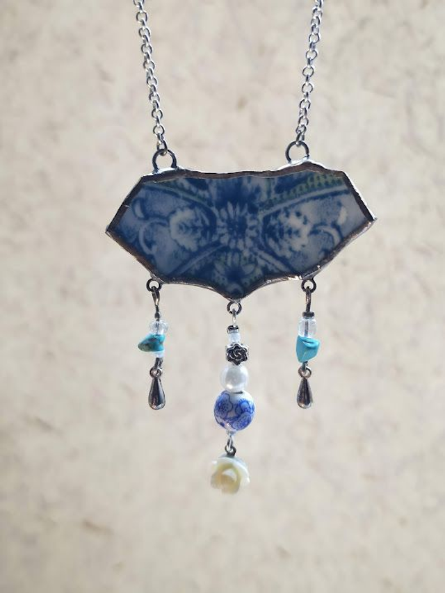 Pendentif en faïence blanche au motif floral bleu avec 3 rangées de perles et chaîne couleur argent serti en Tiffany. Numéro 2