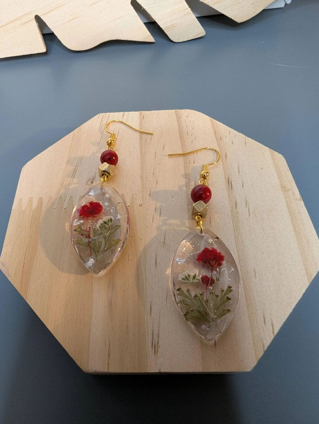 Boucles d&#039;oreilles  avec un pendentif ovale en résine transparente et avec des fleurs séchés, des perle naturelle , le fermoir est en or.