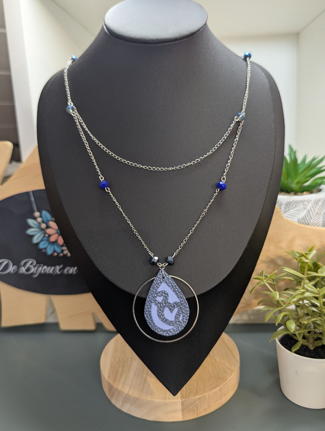 Collier long, sautoir, avec double chaine de couleur argent et un pendentif en cuir et en tissus enduit en forme de goutte et de cœur bleu.