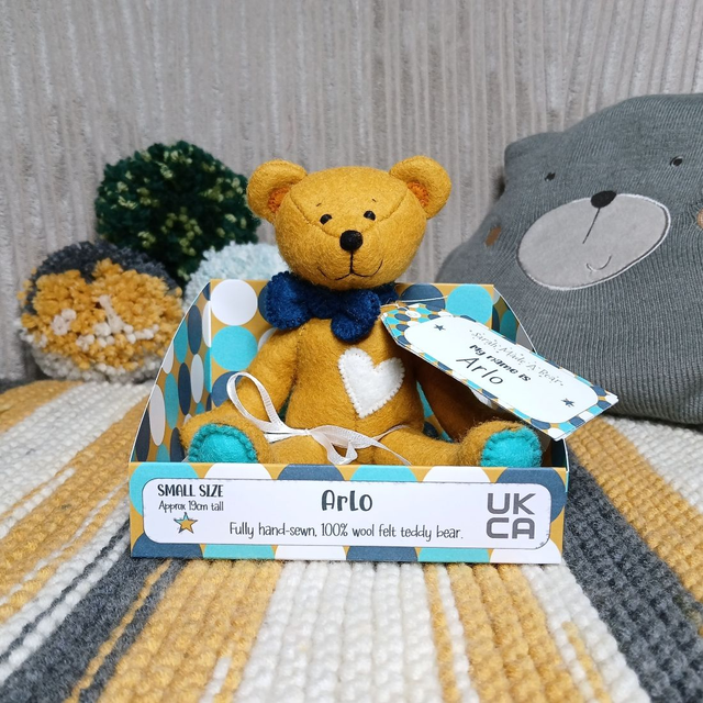 Arlo. Small size, handmade teddy bear. UKCA. Tray base packaging. Standard Wool Felt. Mustard. Dark blue. Turquoise. White.