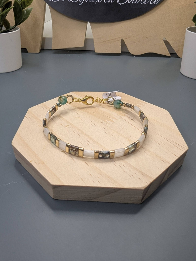 Bracelet avec des perles plate en verre blanches et verts d'eau et des perles en métal doré. Le fermoir et la chaine fermoir sont de couleur or.