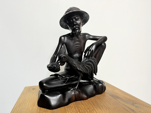 Wooden sculpture of a man feeding a rooster from Tantra Mas Bali Gallery.