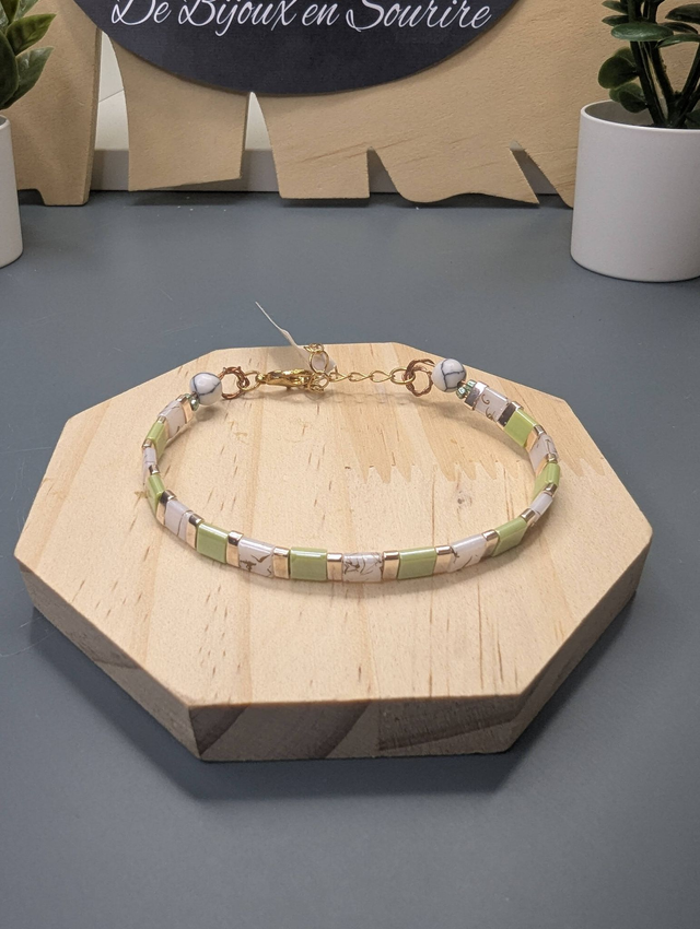 Bracelet avec des perles plate en verre blanches et vertes et des perles en métal doré. Le fermoir et la chaine fermoir sont de couleur or.