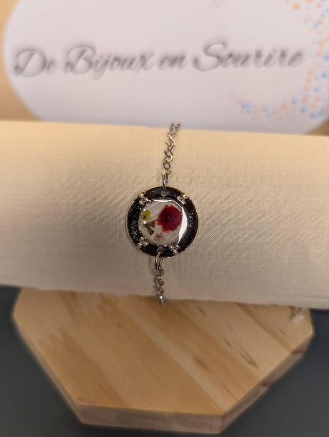 Bracelet avec une chaine en argent, un pendentif en résine noir, avec des fleurs séchés rouge, le fermoir est en argent.