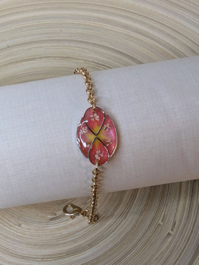 Bracelet ave une chaine de couleur or, pendentif en résine rose et jaune avec des petites fleurs blanches, le fermoir est or.