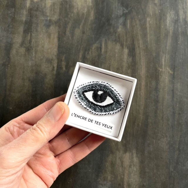 Œil brodé main, présenté dans une boîte comme un talisman