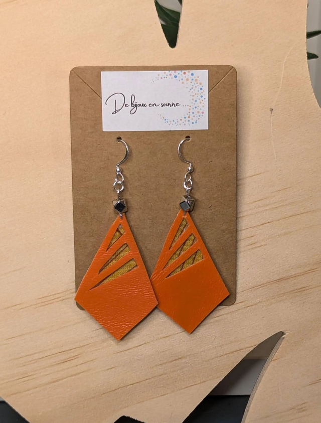 Boucles d'oreilles longue en similicuir orange et tissus enduit, avec des perles métalliques de forme géométrique, le fermoir est en argent. 