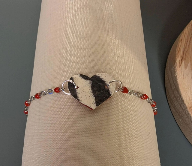 Bracelet en chaine de couleur argent et cœur en cuir et tissus enduit rouge, le fermoir est de couleur argent. 