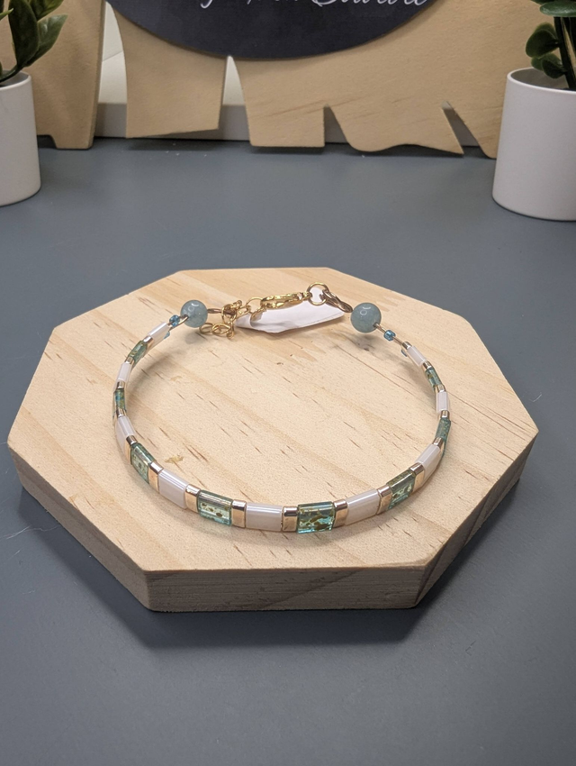 Bracelet avec des perles plate en verre blanches et bleu et des perles en métal doré. Le fermoir et la chaine fermoir sont de couleur or.