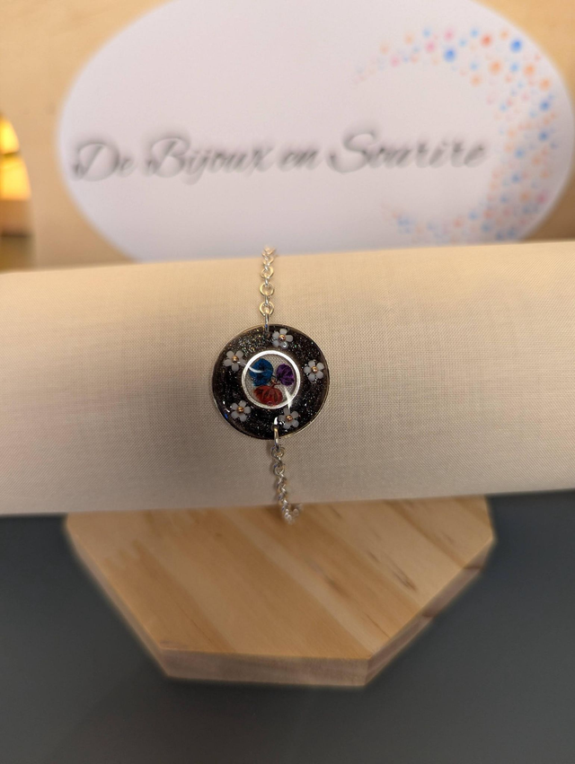  Bracelet avec une chaine de couleur argent, un pendentif en résine noir avec des fleurs séchés, le fermoir est en argent.
