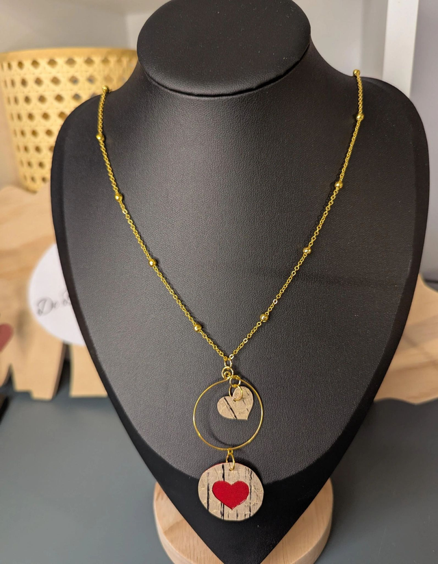 Collier long, sautoir, avec une chaine de couleur or et un pendentif en cuir et en tissus enduit en forme de rond et de cœur.