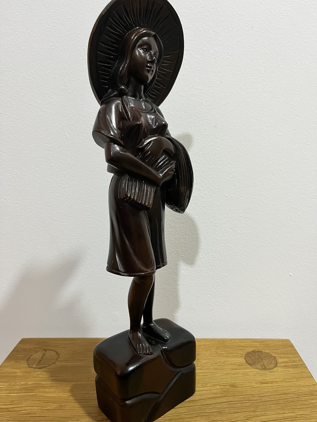 A wooden statue of a Filipino female farmer, with a hat, holding harvested rice.
